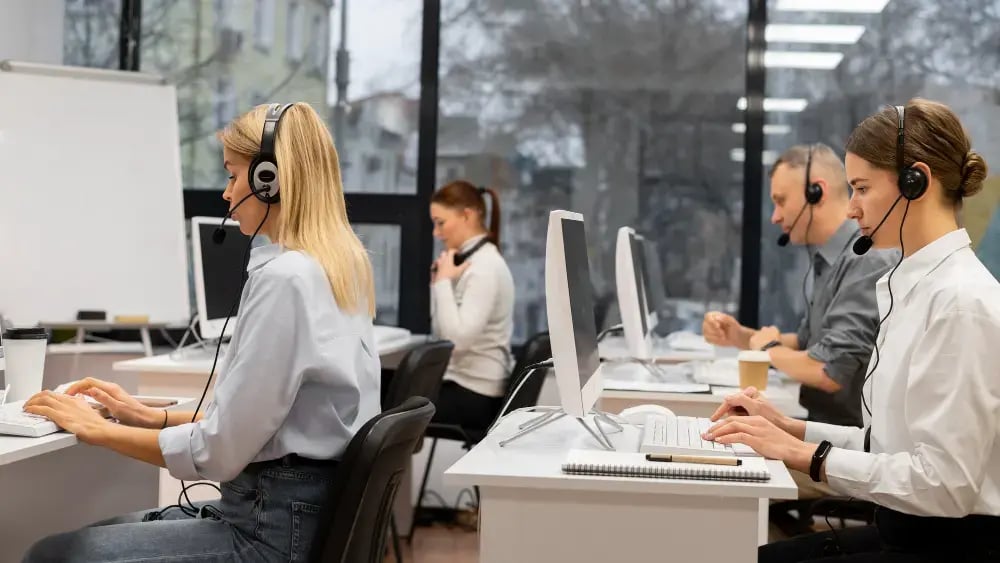 Agentes de call center usando fones de ouvido e computadores em um escritório moderno, demonstrando habilidades essenciais de atendimento ao cliente e comunicação
